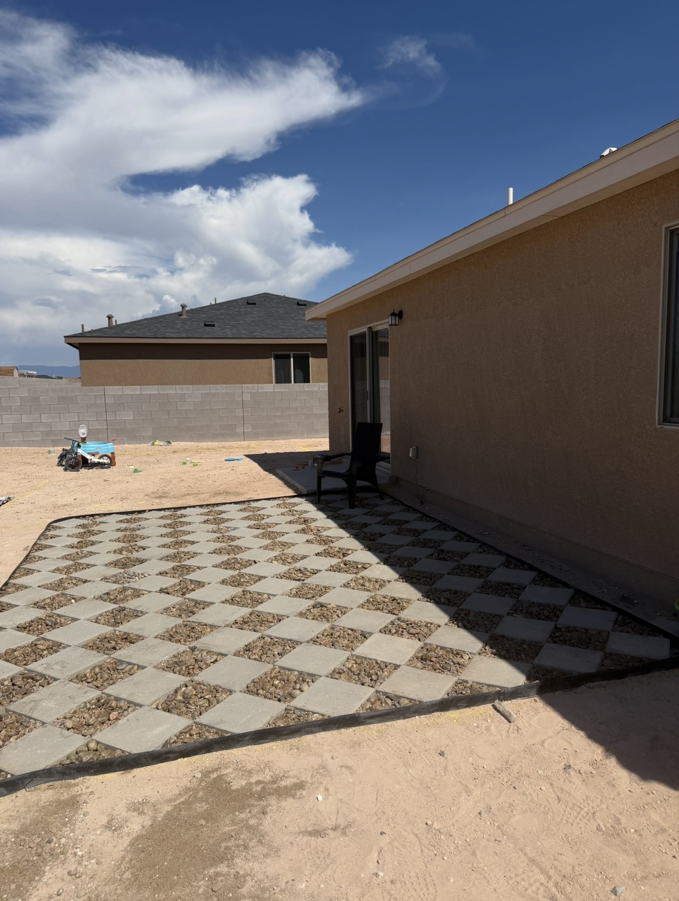 Checkerboard paver and gravel patio installed next to a stucco home